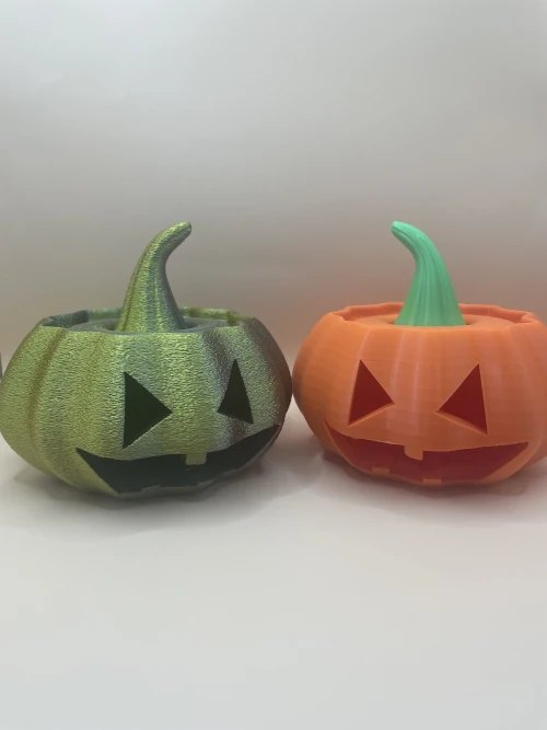 Deux citrouilles d'Halloween décoratives imprimées en 3D, l'une orange et l'autre vert métallisé, avec visage sculpté.