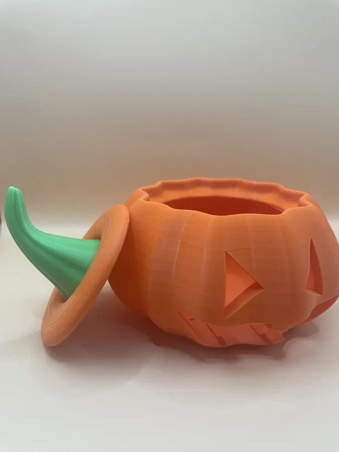 Deux citrouilles d'Halloween décoratives imprimées en 3D, l'une orange et l'autre vert métallisé, avec visage sculpté.