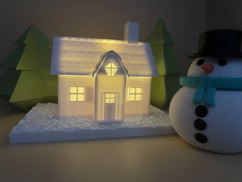 Maison de Noël imprimée en 3D, éclairage LED intérieur, avec bonhomme de neige et sapins décoratifs.