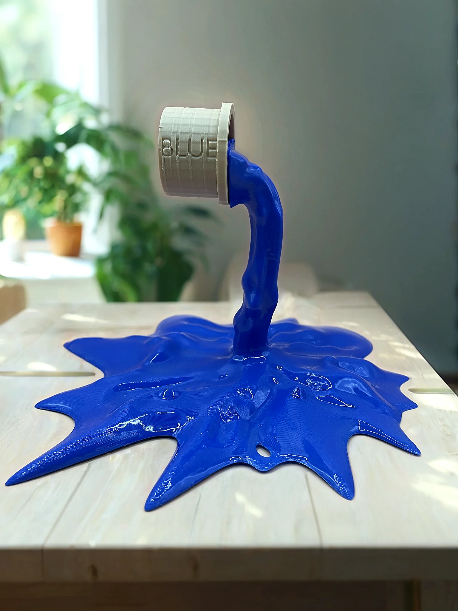 Sculpture imprimée en 3D représentant un pot de peinture renversé formant une éclaboussure bleue.