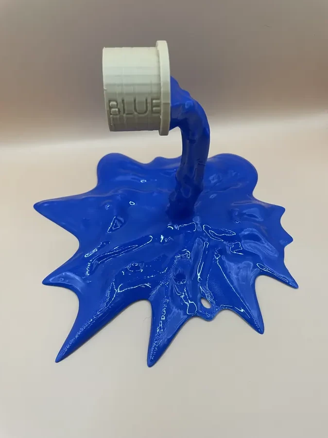 Sculpture imprimée en 3D représentant un pot de peinture renversé formant une éclaboussure bleue.