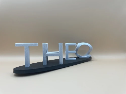 Ambigramme personnalisé imprimé en 3D : lettres argentées en volume posées sur un socle noir, formant un prénom décoratif.