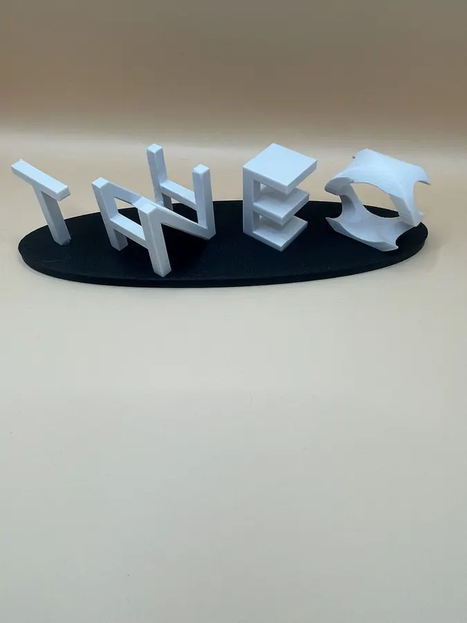Ambigramme personnalisé imprimé en 3D : lettres argentées en volume posées sur un socle noir, formant un prénom décoratif.